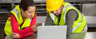 Male and female workers using laptop in factory